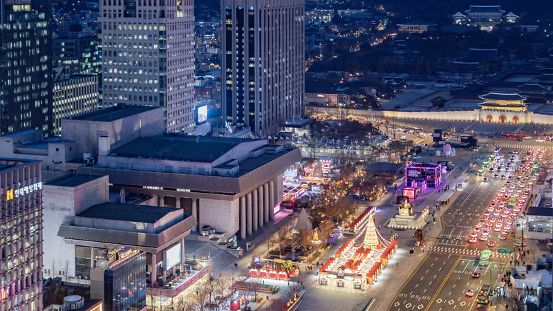 Gwanghwamun Square lit up at night between Seoul office towers, with Gwanghwamun Gate glowing at the far end