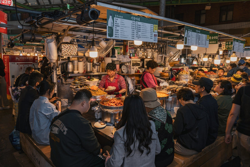 Diners crowded along a Gwangjang Market stall counter as cooks serve hot dishes