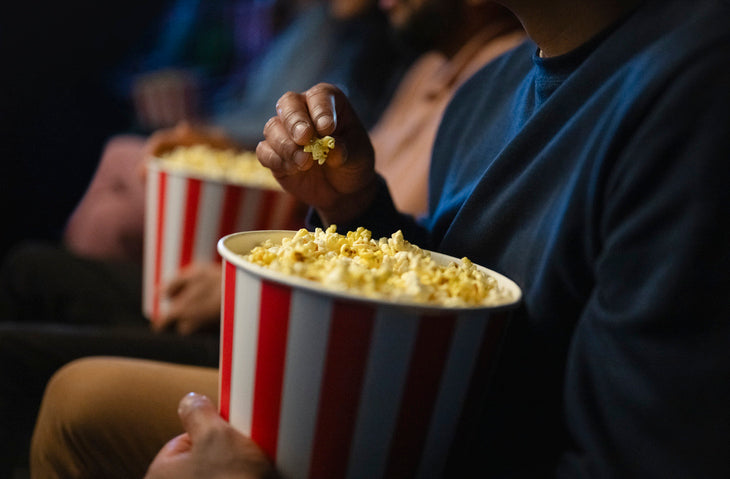 Moviegoers holding striped popcorn buckets in a dark cinema