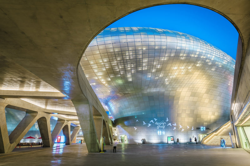 Dongdaemun Design Plaza curved silver facade framed by its concrete arches at dusk