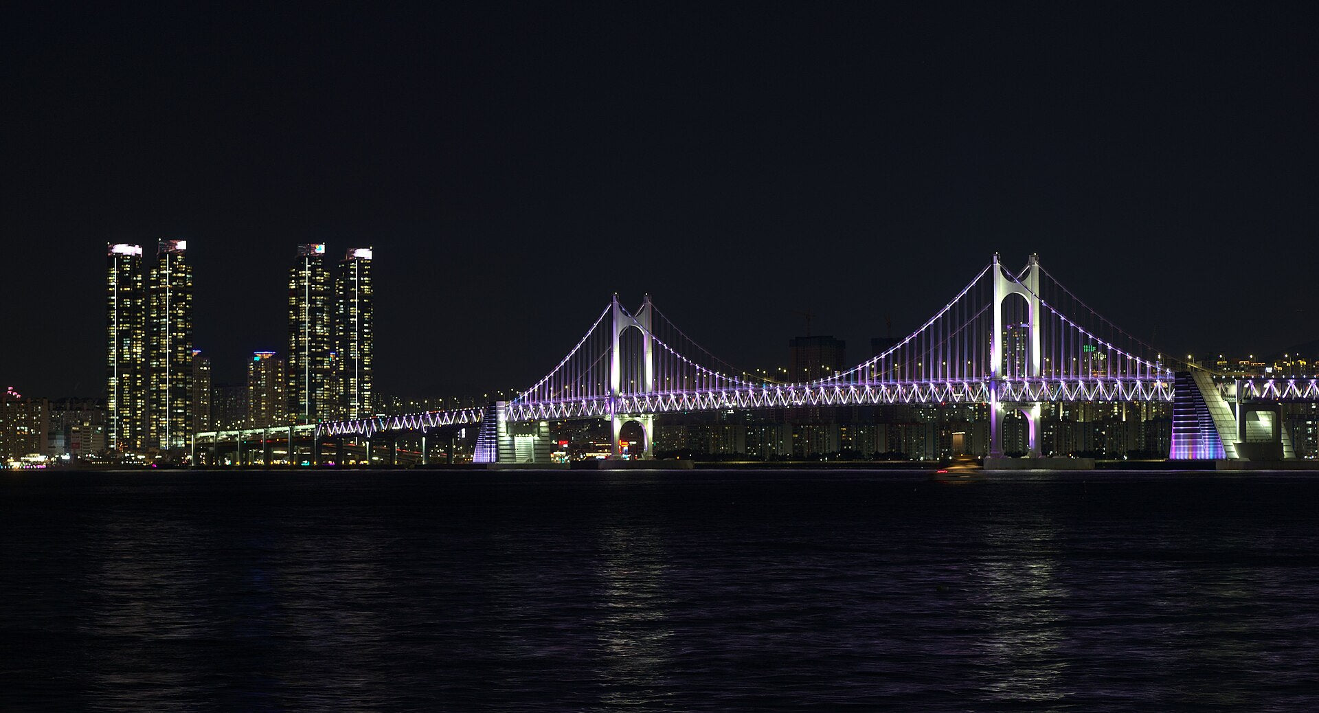 Gwangan Bridge lit in purple at night with Marine City towers glowing beside it