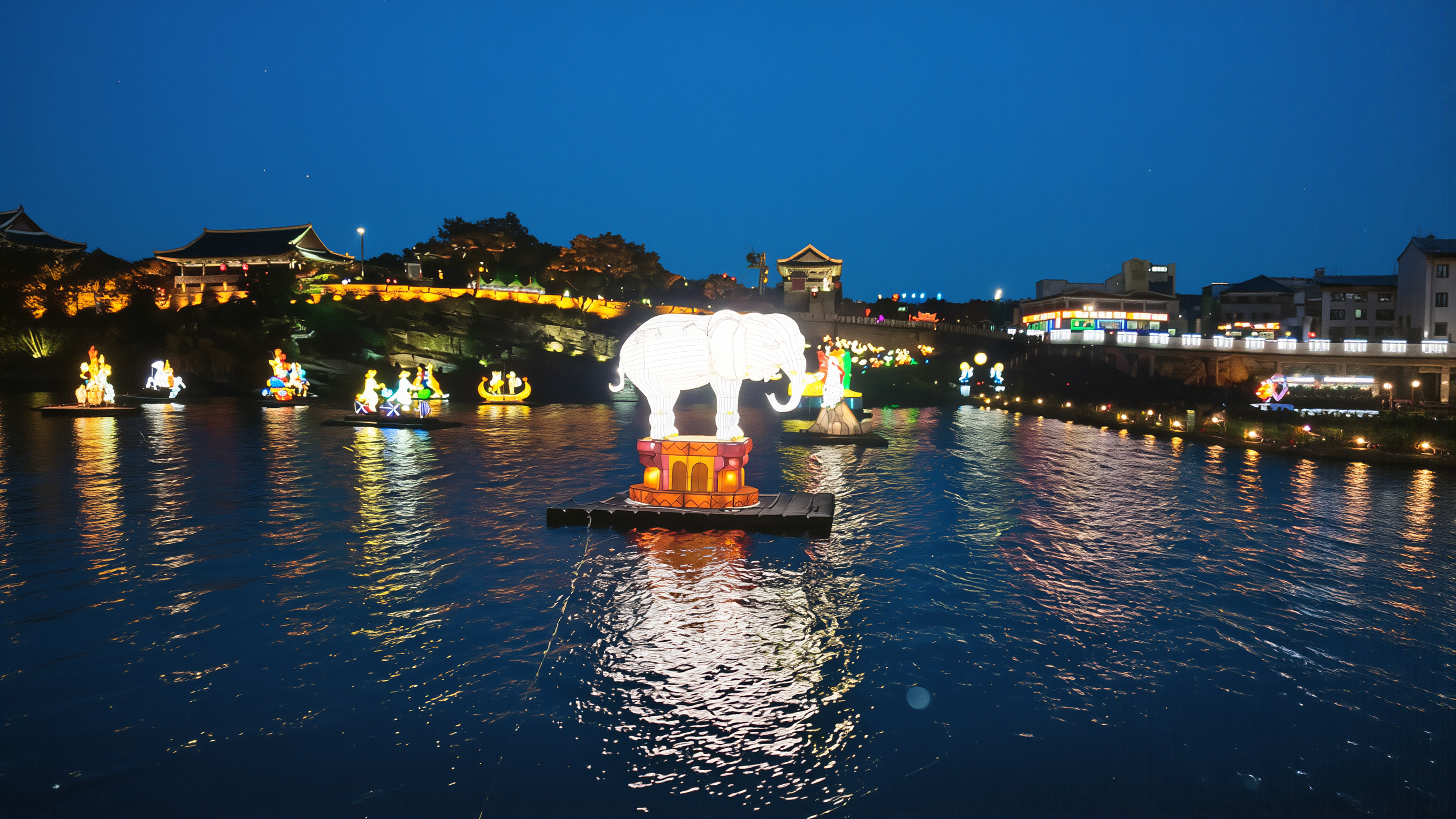 Jinju Lantern Festival white elephant lantern floating on the Namgang River below the lit fortress walls at blue hour