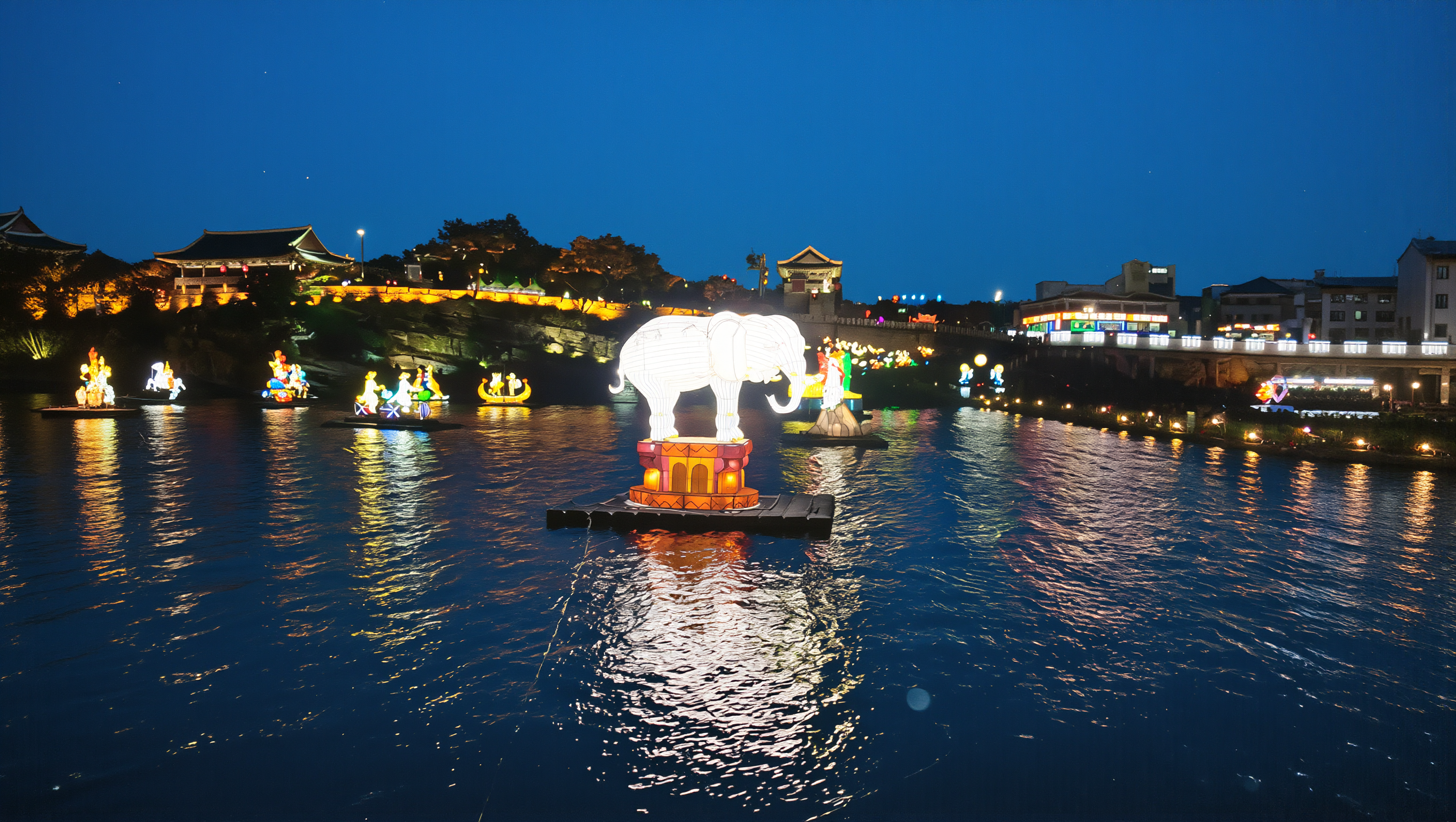 Jinju Lantern Festival white elephant lantern floating on the Namgang River below the lit fortress walls at blue hour