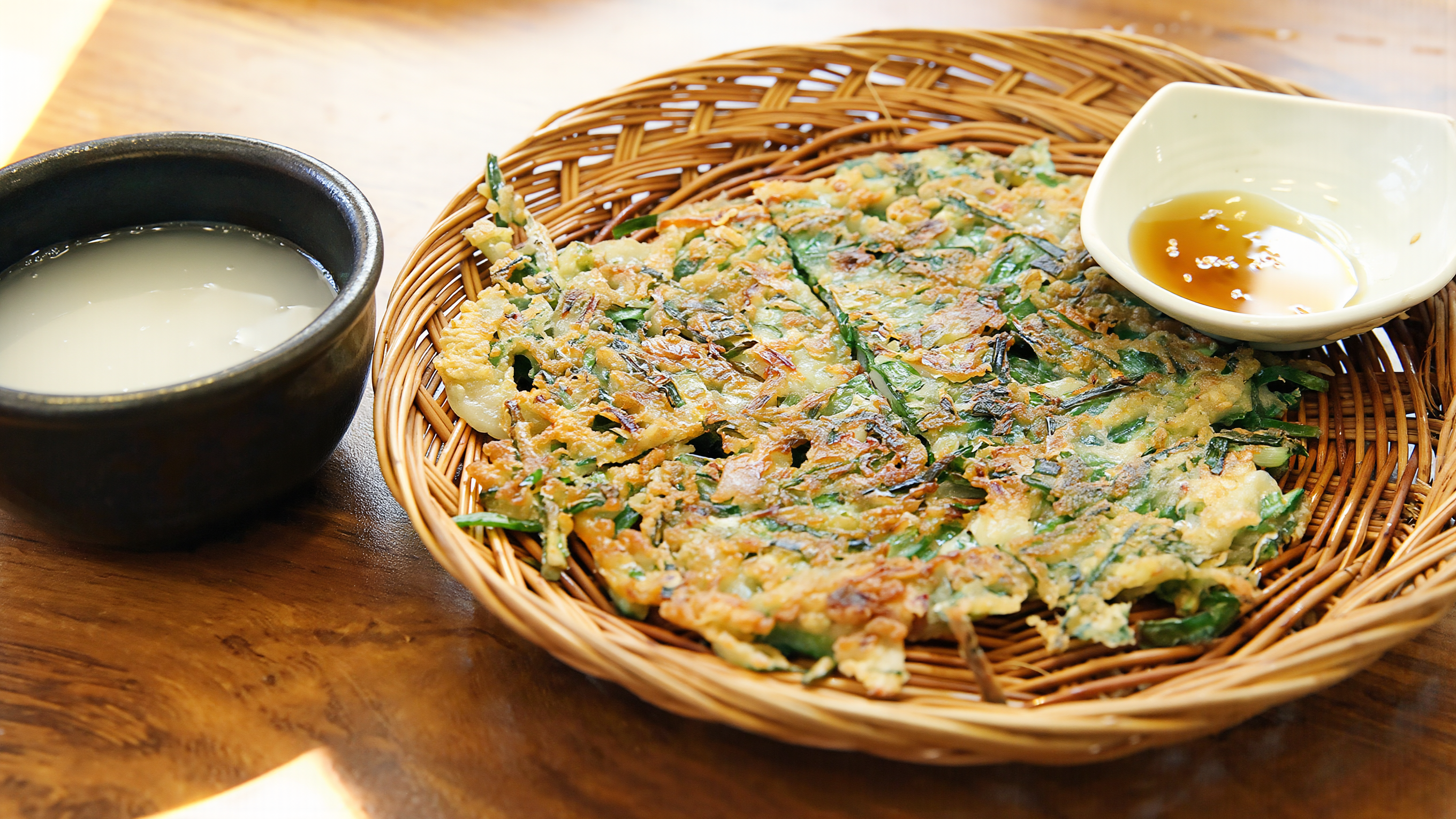 Makgeolli in a stoneware cup beside a crisp scallion pancake, a classic pairing in Korean drinking culture