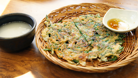 Makgeolli in a stoneware cup beside a crisp scallion pancake, a classic pairing in Korean drinking culture