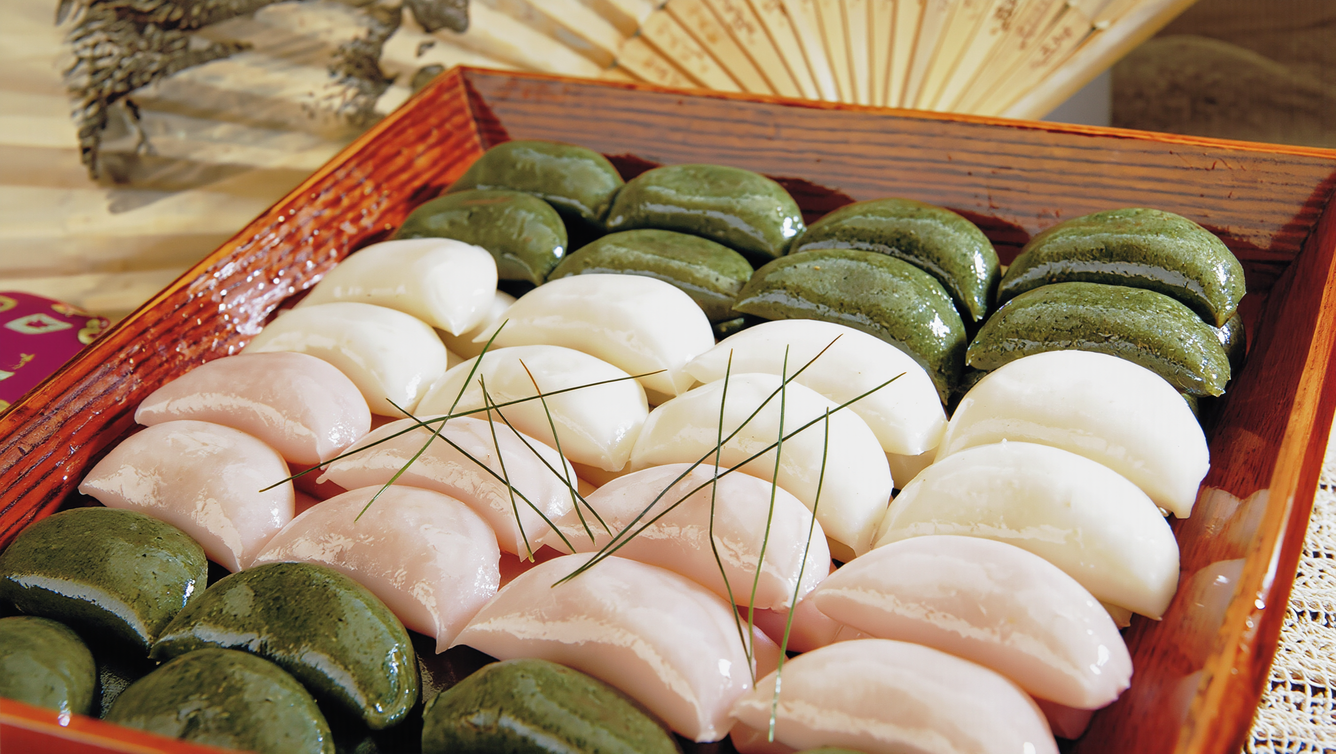 Green, white and pink half-moon songpyeon lined up on a lacquered wooden tray with pine needles for Chuseok
