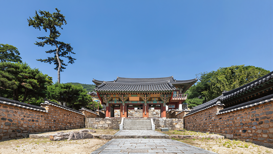 Stone path leading to the painted wooden gate of a Korean mountain temple under clear blue sky