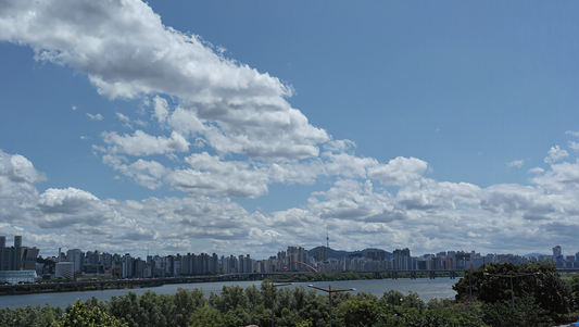 The Han River in Seoul on a clear summer day, city skyline and Namsan tower on the far bank under drifting cumulus