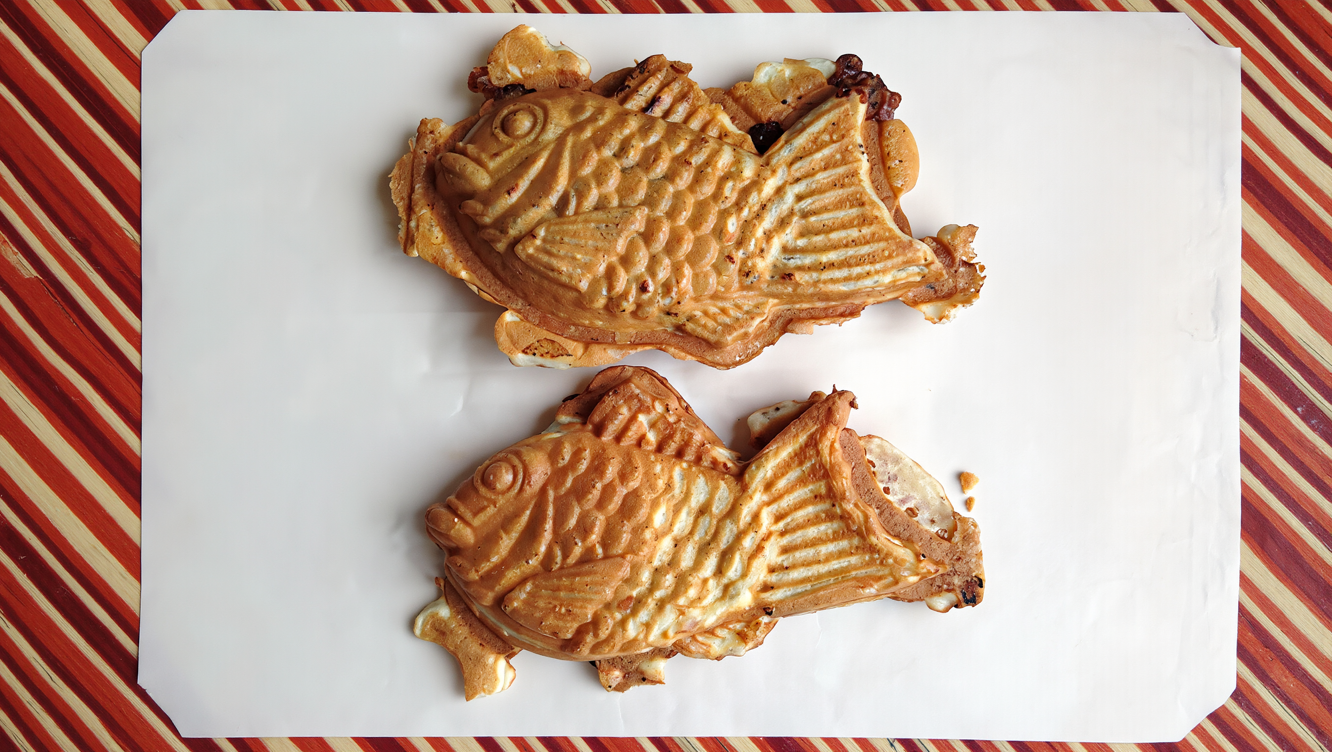 Two golden bungeoppang fish pastries side by side on white paper over a striped tablecloth