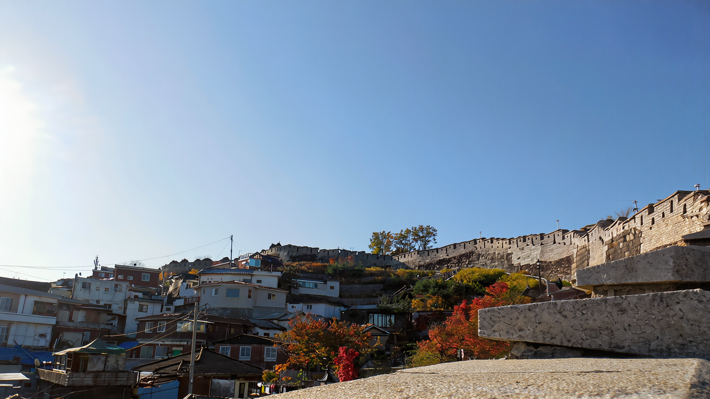 The old Seoul city wall along a ridge above hillside houses under a clear blue autumn sky