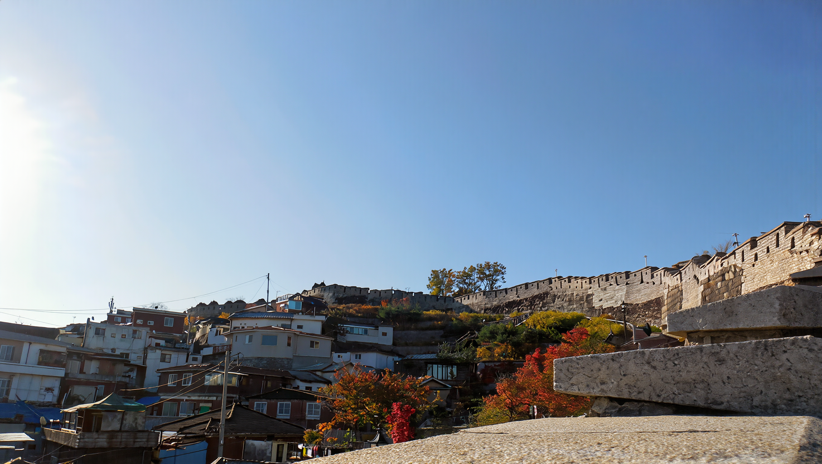 The old Seoul city wall along a ridge above hillside houses under a clear blue autumn sky