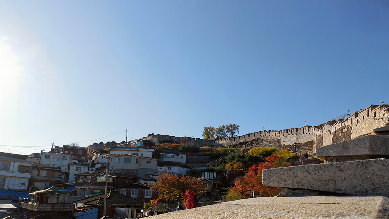 The old Seoul city wall along a ridge above hillside houses under a clear blue autumn sky