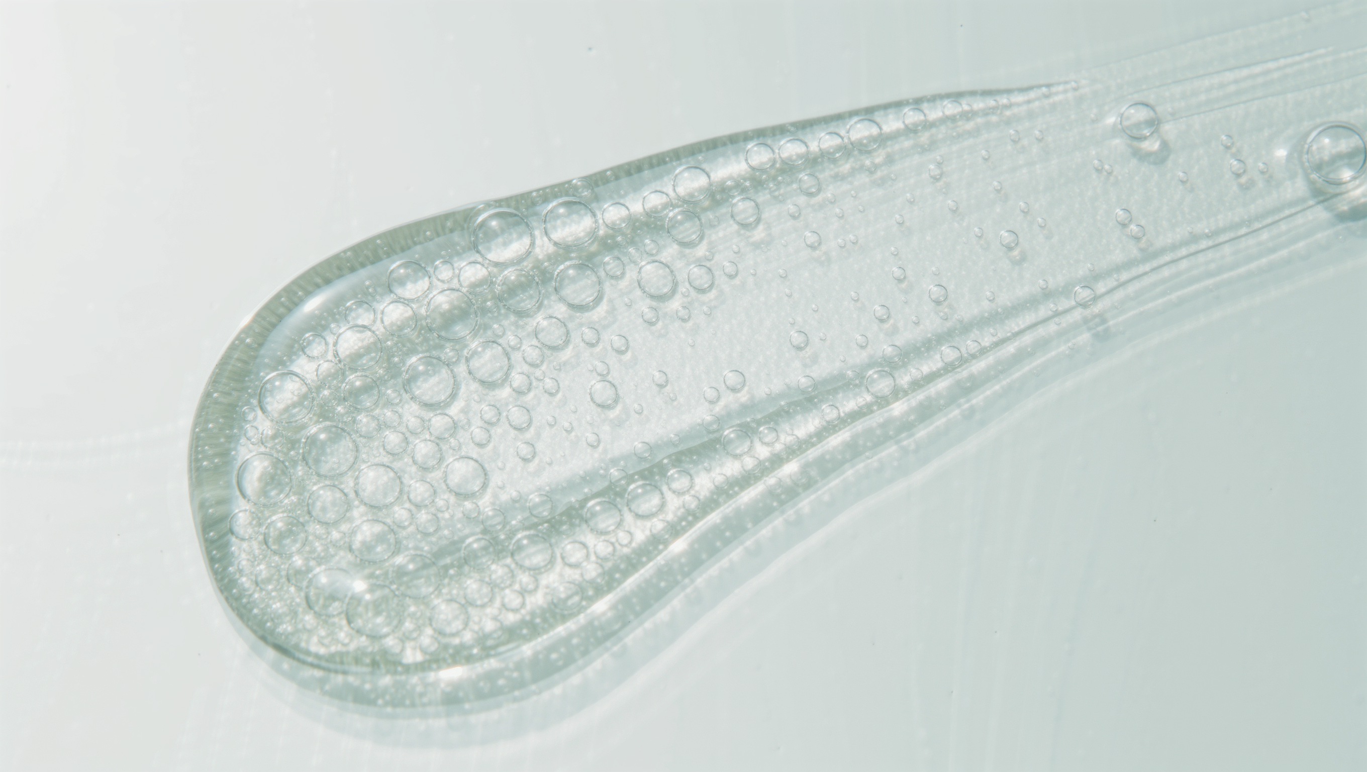 Glossy clear serum gel swipe with fine bubbles on a bright pale surface