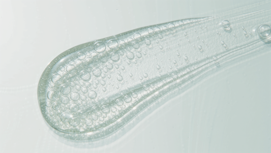 Glossy clear serum gel swipe with fine bubbles on a bright pale surface