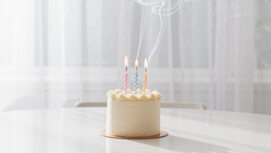 Small cream birthday cake with three lit candles on a bright table, one for each of Korea's three age systems