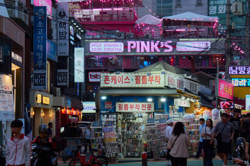 Neon signs and rooftop terraces lighting up a Hongdae shopping street at dusk