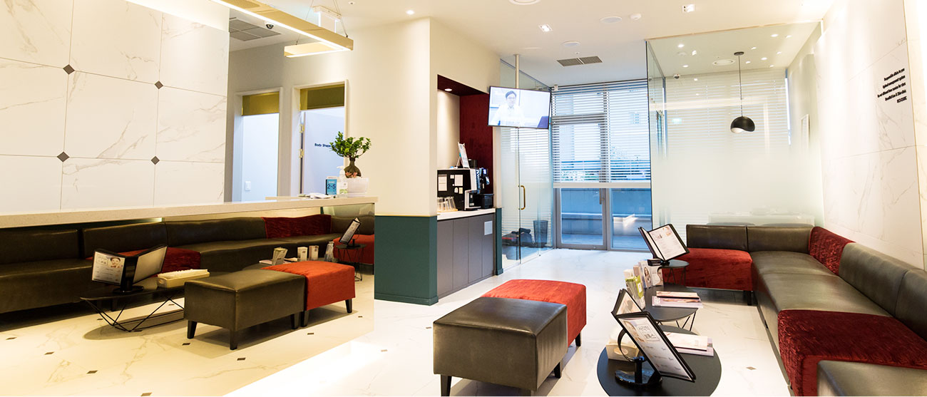 Dermatology clinic in Seoul: a bright reception lobby with red and charcoal sofas, marble floors and glass doors