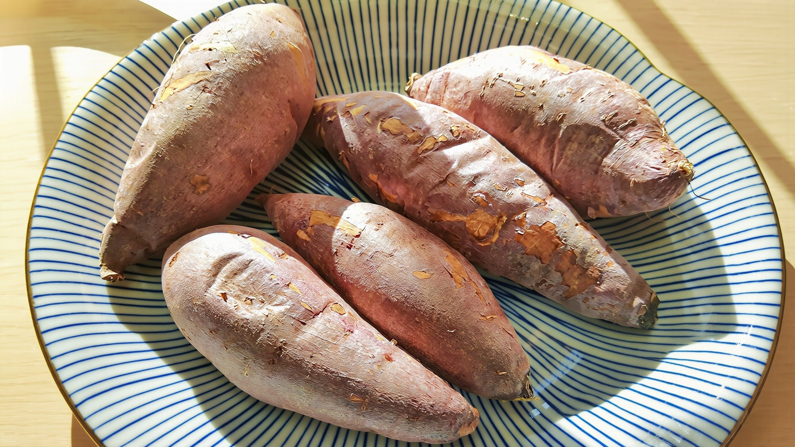 Roasted Korean sweet potatoes with thin reddish skins on a striped ceramic plate in soft morning light