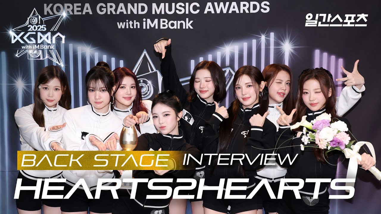 Hearts2Hearts holding trophies backstage at the 2025 Korea Grand Music Awards (KGMA Official YouTube)