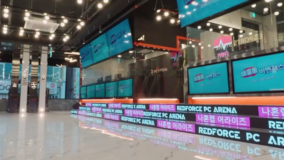 Bright PC bang interior with wall-mounted screens, neon esports signage and a glossy floor reflecting the lights