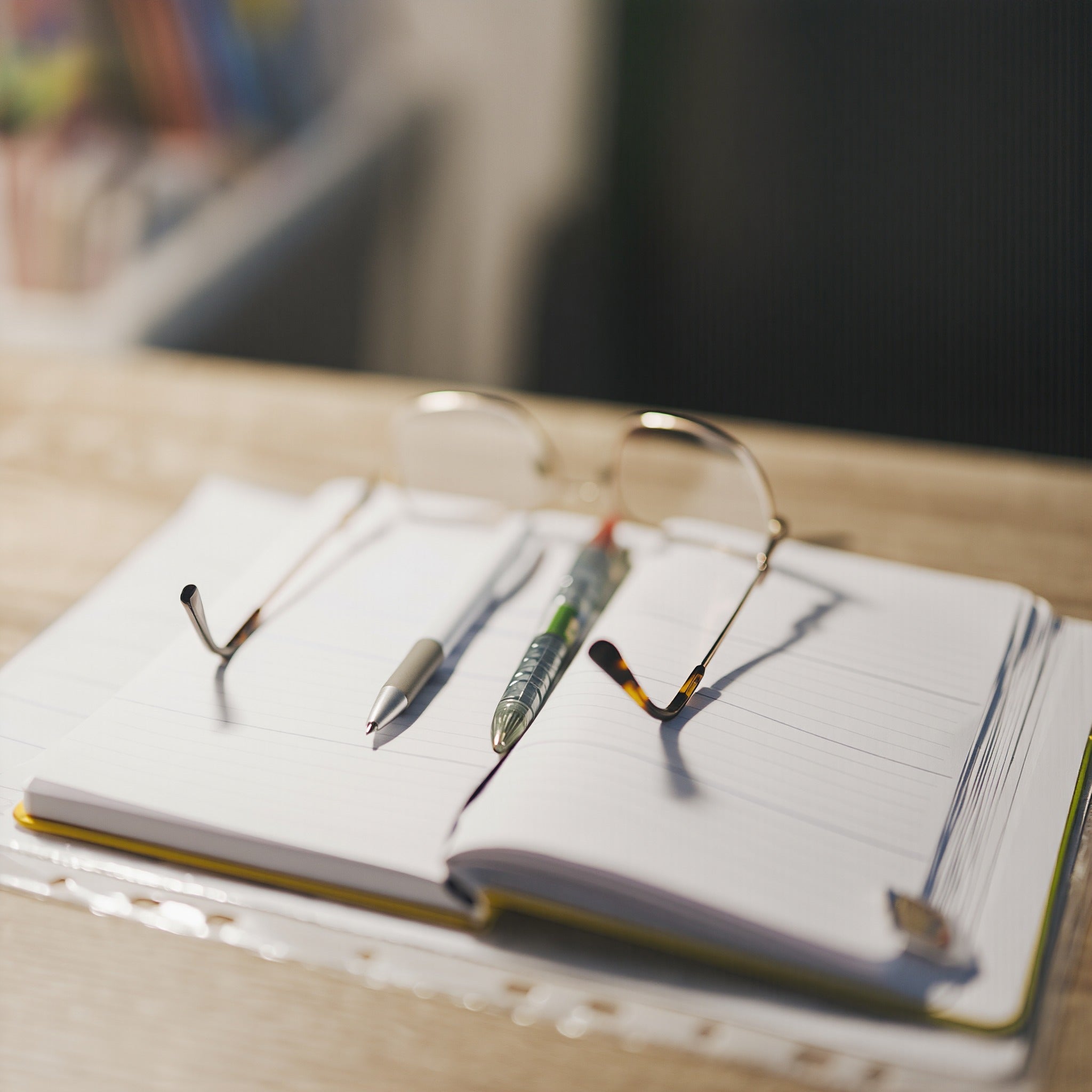 Open notebook with two pens and wire-rimmed glasses on an editor's desk in morning light